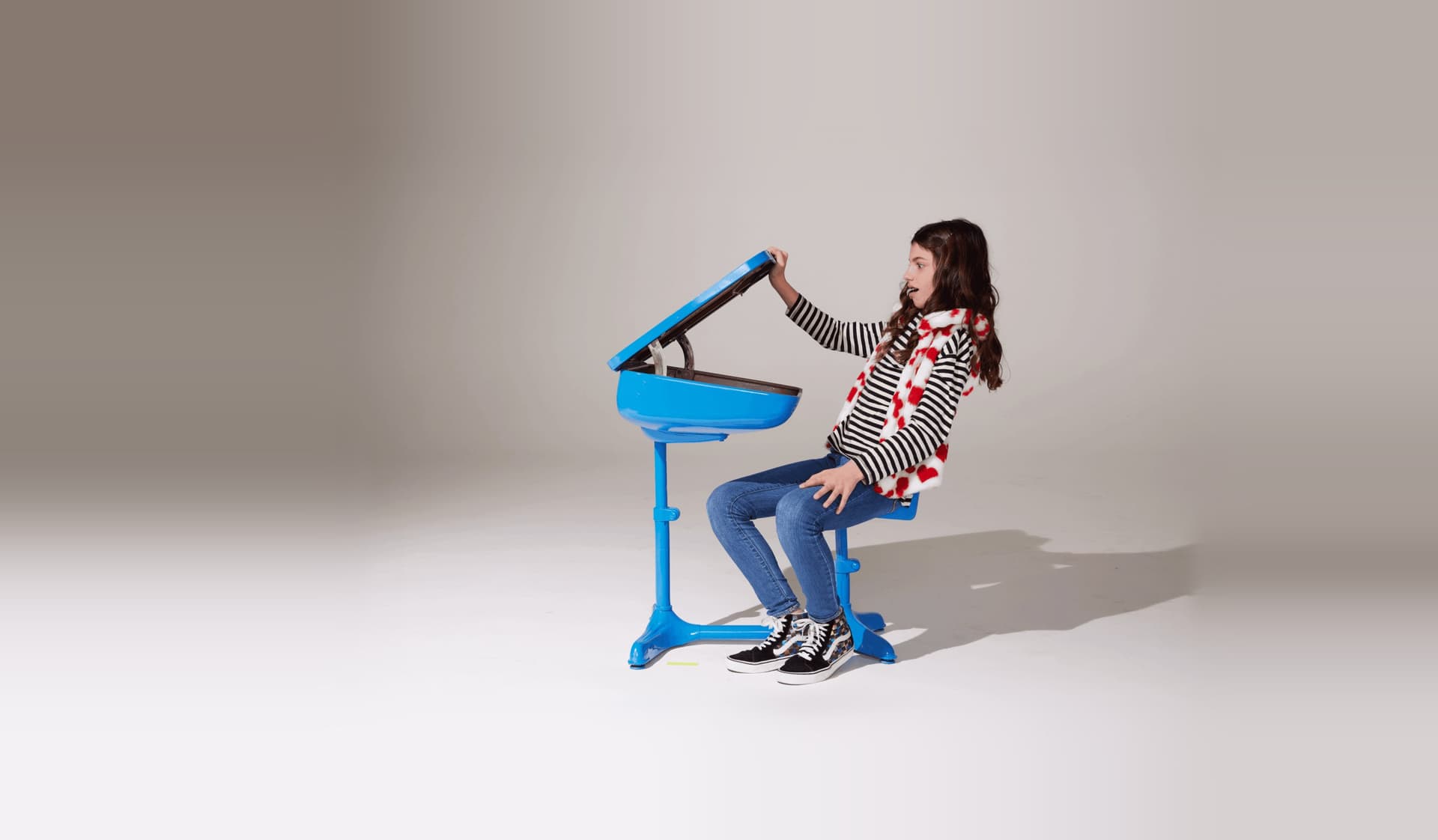 Raw studio shot of a girl lifting the lid of a blue desk